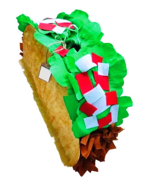 Piñata en forma de taco gigante, con la tortilla dorada de flecos, lechuga de papel verde rizado y confeti rojo y blanco, recortada sobre fondo liso.